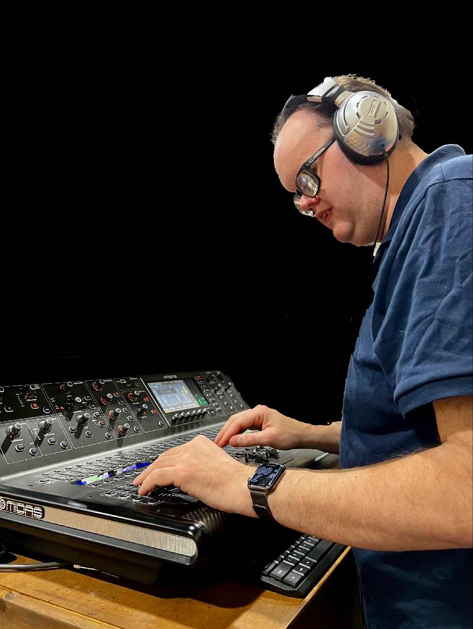 James is stood in front of a soundboard adjusting levels